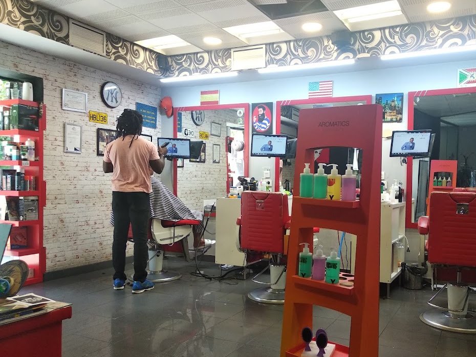 Interior de la barbería con sillones rojos, espejos y pared de ladrillo blanco